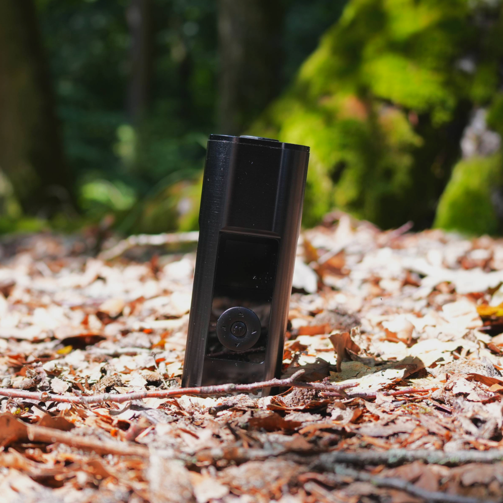 Tragbarer Vaporizer mit digitalem Display steht auf Laub im sonnendurchfluteten Wald