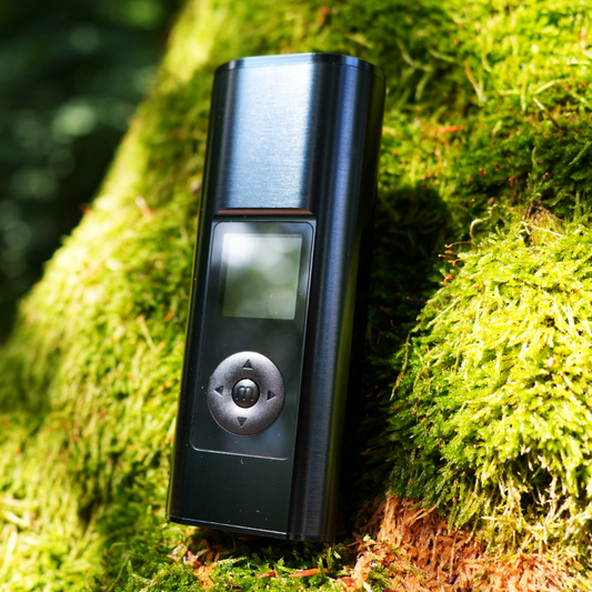Arizer Solo 3 V2 mit LCD-Anzeige und Steuerknopf in direkter Frontalansicht auf einem mit Moos bedeckten Baum im Wald