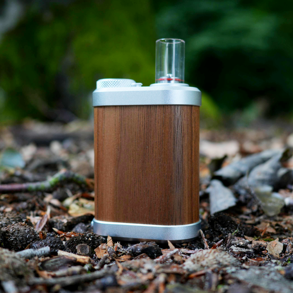 Zeigt den Tinymight V 2 Vaporizer auf Waldboden stehend mit moosbedecktem Baum im Hintergrund.